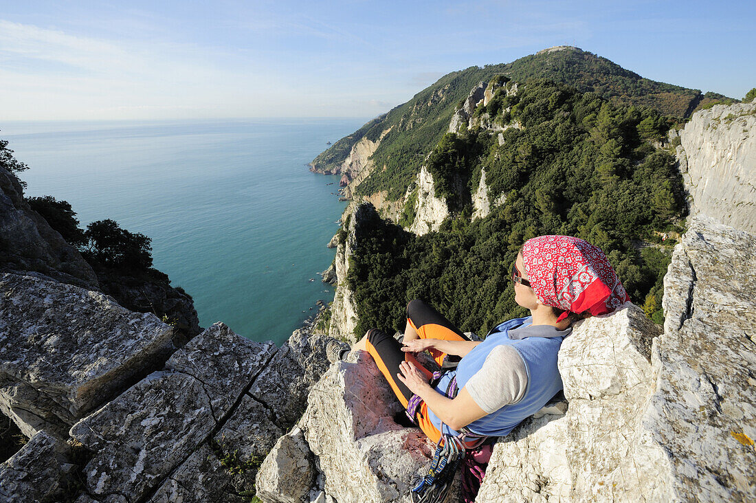 Frau mit Kletterausrüstung blickt auf Felsabbrüche an der Mittelmeerküste, Naturpark Porto Venere, Nationalpark Cinque Terre, UNESCO Welterbe, Ligurien, Italien