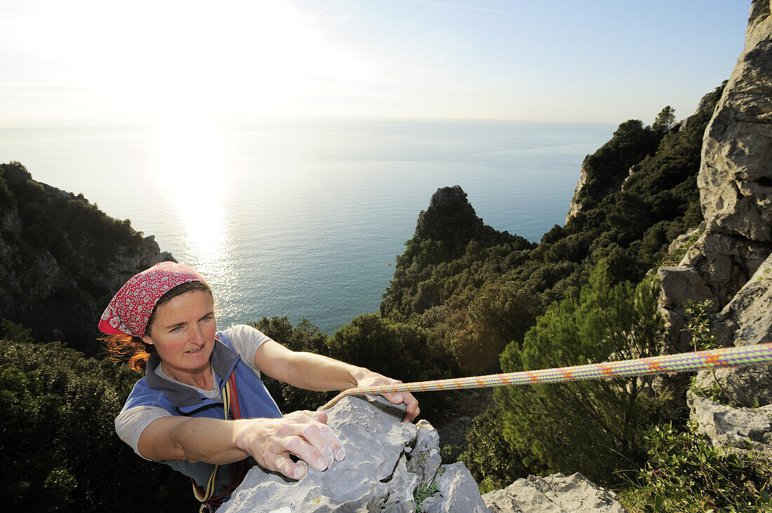 Frau klettert an Felswand hoch über der Mittelmeerküste, Naturpark Porto Venere, Nationalpark Cinque Terre, UNESCO Welterbe, Ligurien, Italien