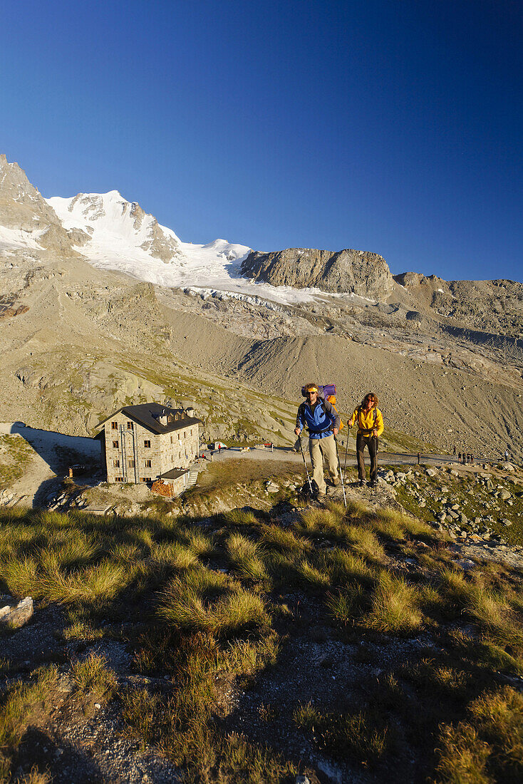 Couple hiking, Rifugio Chabod and Gran Paradiso in background, Gran Paradiso National Park, Aosta Valley, Italy