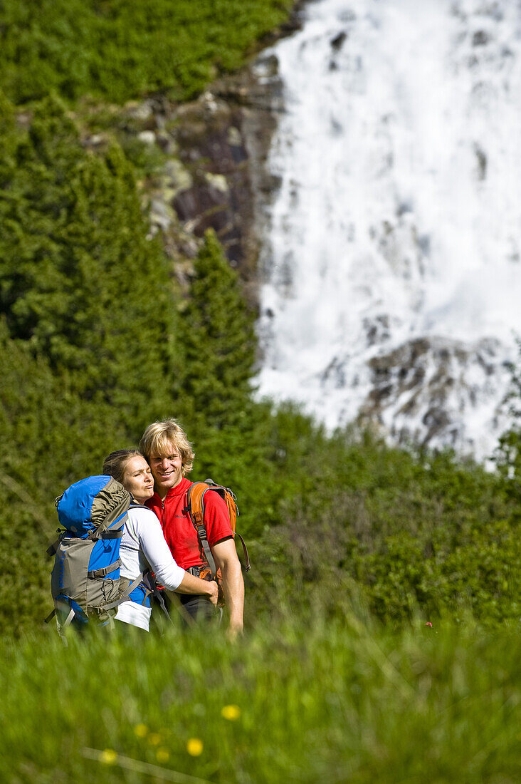 Paar umarmt sich auf einer Wiese, Wasserfall im Hintergrund, Zillertal, Tirol, Österreich