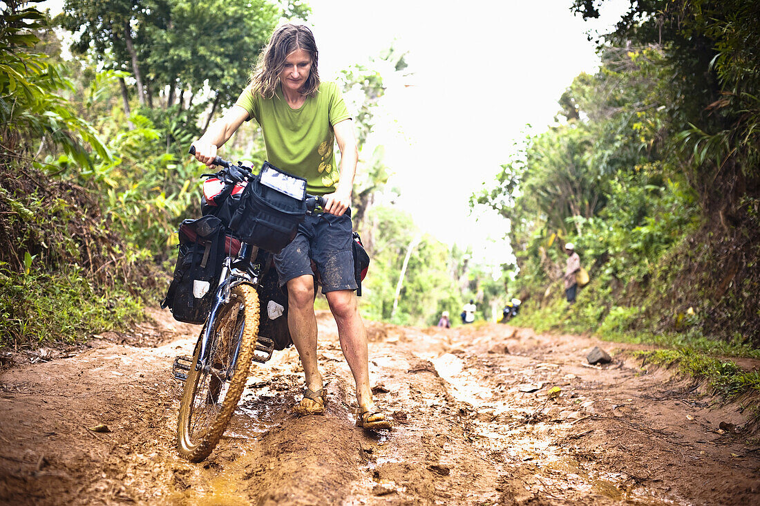 Frau schiebt Mountainbike durch Schlamm, Nationalpark Masoala, Madagaskar