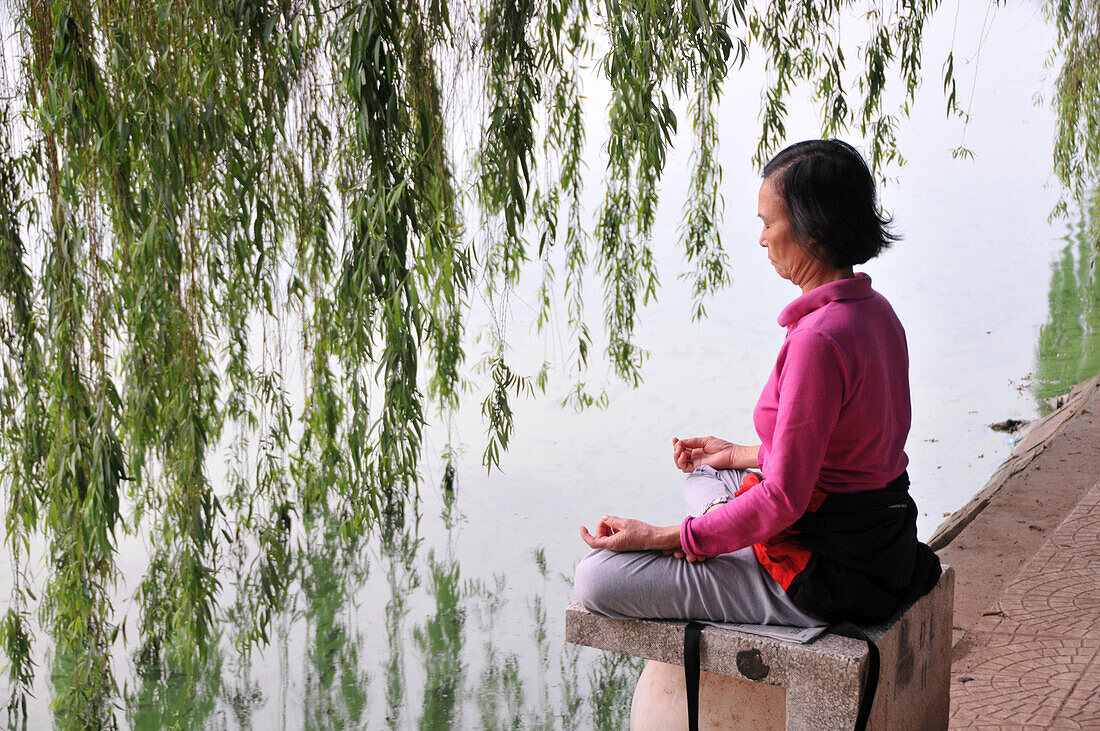 Woman doing yoga exercises near Hoan Kiem lake, old town of Hanoi, Vietnam