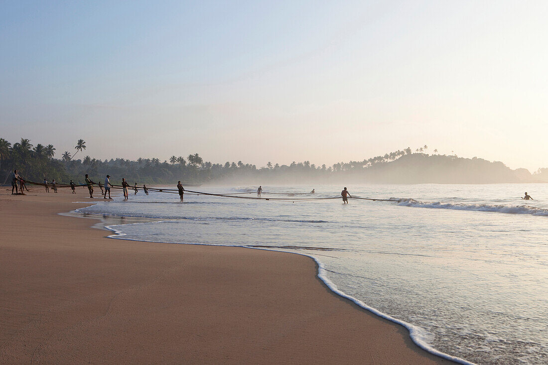 Fischer im Morgenlicht am Strand von Talalla holen ihr Netz ein, Talalla, Matara, Südküste, Sri Lanka, Asien