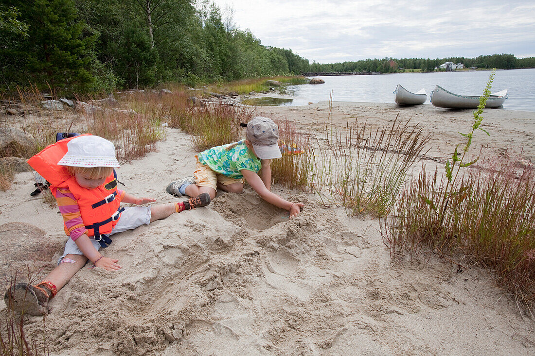 Zwei Mädchen spielen am Strand, im Hintergrund zwei Kanus, Insel Norrbyskär, Västerbotten, Schweden, Europa