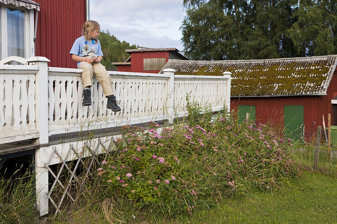 Ein Mädchen sitzt auf dem Geländer eines Bauernhauses, Västernorrland, Schweden, Europa