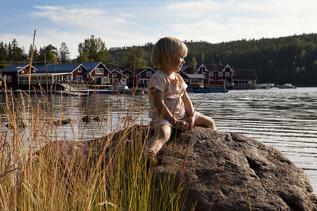 Ein kleines Mädchen auf einem Felsen vor dem Dorf Norrfällsviken, Höga Kusten, Västernorrland, Schweden, Europa