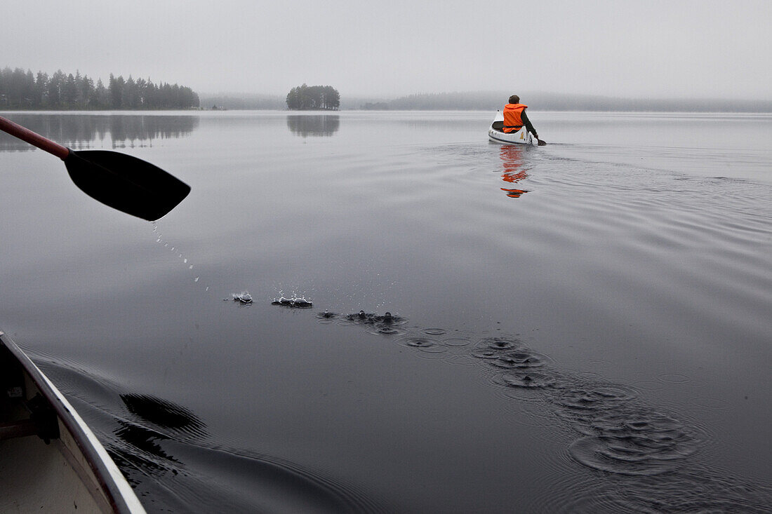 Two men in canoes on the lake of Trehörningsjö, Vaesternorrland, Sweden, Europe
