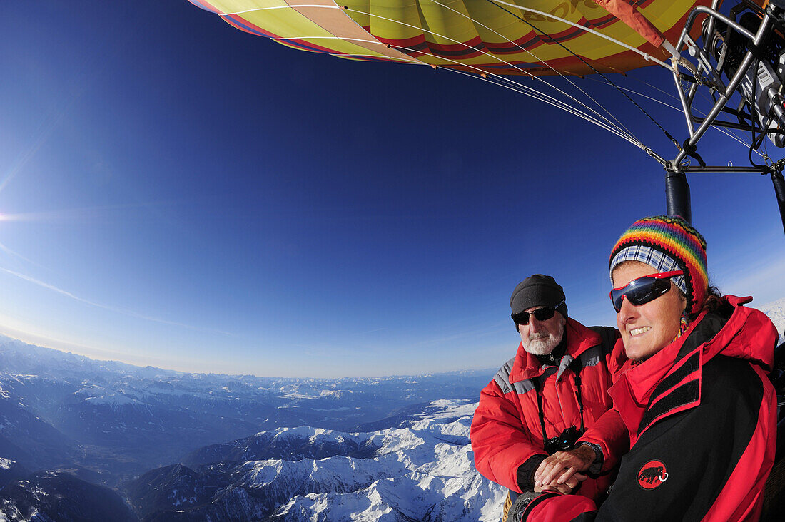Zwei Personen in Heißluftballon genießen Blick auf verschneite Alpen, Luftaufnahme, Südtirol, Italien, Europa