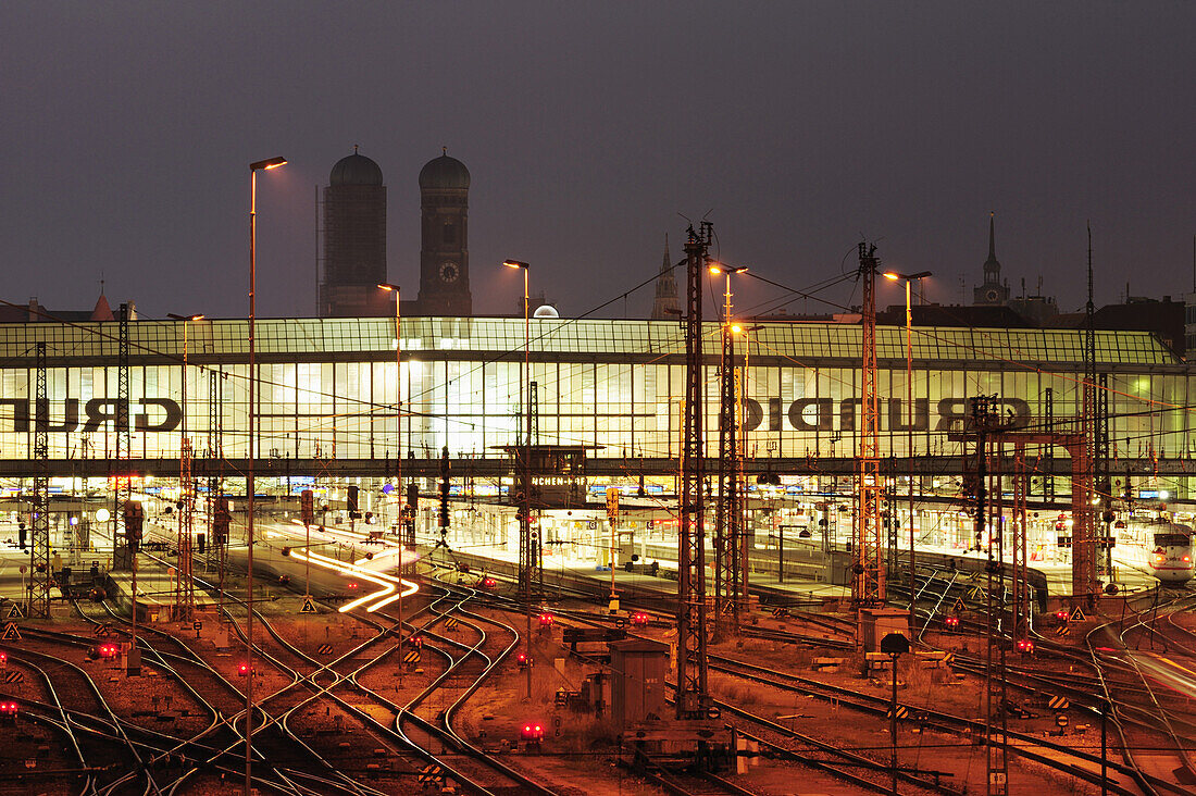 Schienen und Bahnhofsgebäude, beleuchtet, Frauenkirche im Hintergrund, Hauptbahnhof München, München, Oberbayern, Bayern, Deutschland