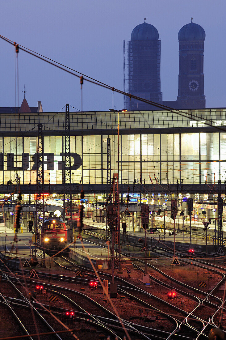 Illuminated tracks, trains and railway building, twin towers of the Frauenkirche cathedral in the background, Munich main station, Munich, Upper Bavaria, Bavaria, Germany