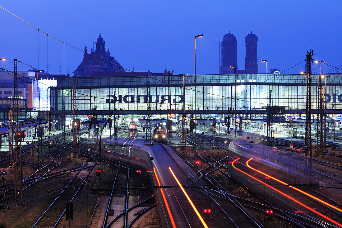 Illuminated tracks and railway building, twin towers of the Frauenkirche and palace of justice in the background, Munich main station, Munich, Upper Bavaria, Bavaria, Germany