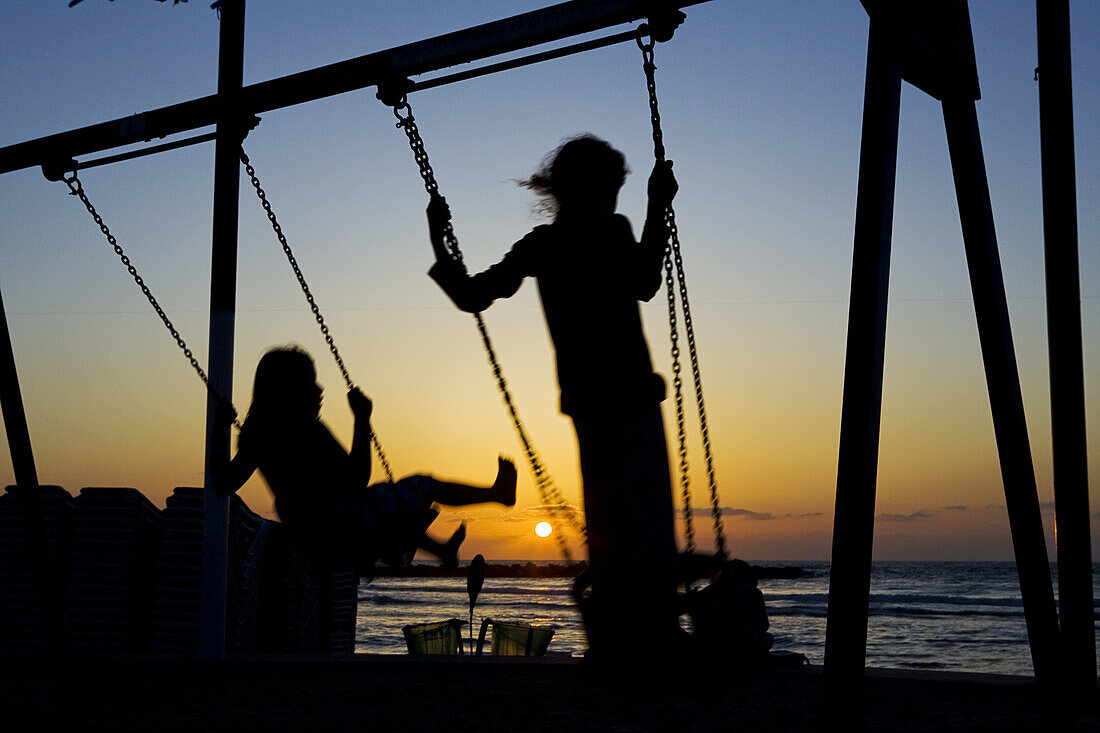 Girls on swings on Mezizim Beach at sunset, Tel Aviv, Israel, Middle East