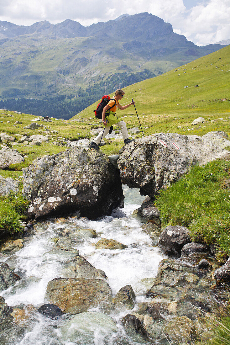 Wanderin überquert Bach im Val da Natons, Kanton Graubünden, Schweiz