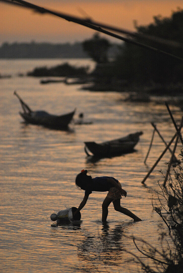 Mädchen holt Wasser mit Gießkanne aus dem Mekong Fluss bei Sonnenaufgang, Champasak, im Süden von Laos, Asien