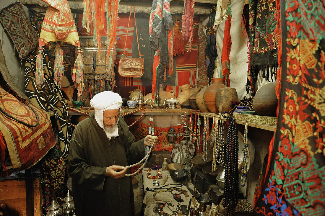 Verkäufer in seinem Geschäft mit typischen Waren aus der Sahara im Souk in Marrakesch, Marokko, Afrika