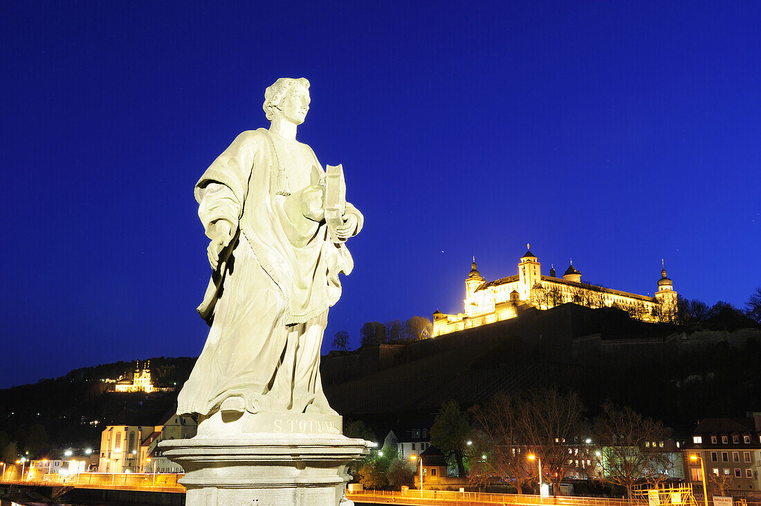 Illuminated statue on the Alte Mainbruecke bridge with illuminated castle, Feste Marienberg, in the background, night shot, Wuerzburg, Bavaria, Germany