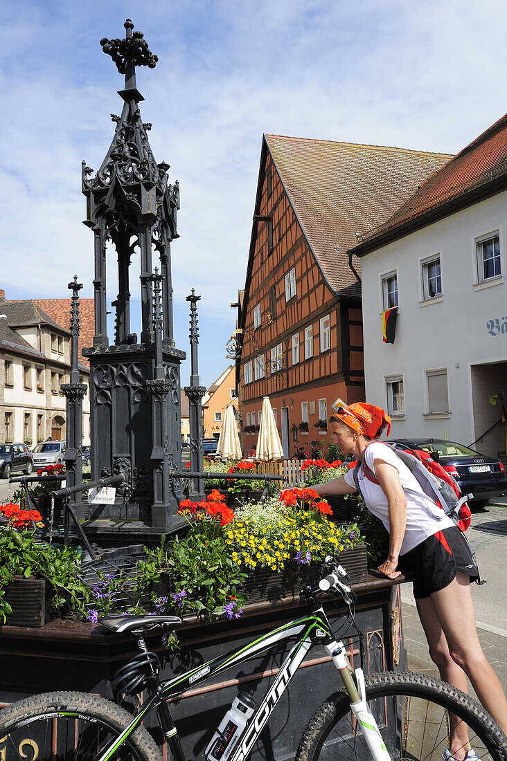 Female cyclist refreshing at fountain Roehrenbrunnen, Leutershausen, Altmuehltal cycle trail, Bavaria, Germany