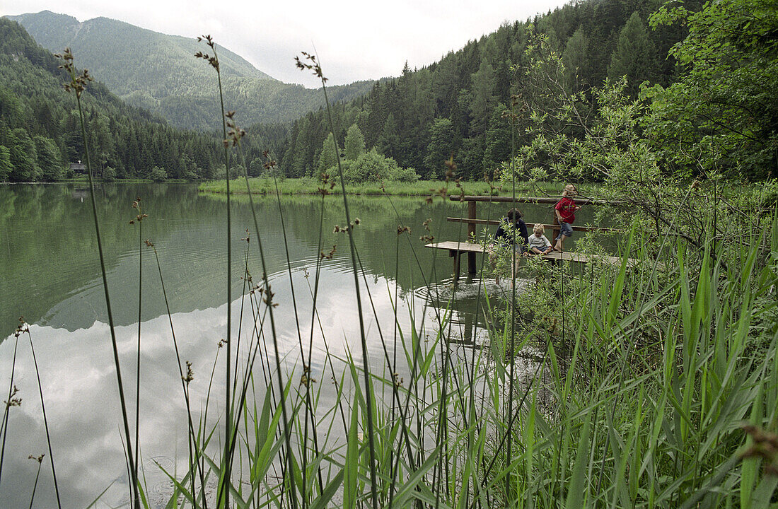 Eine Mutter mit zwei Kinder sitzen auf einem Steg am See, Schaffner Weiher, Stodertal, Oberösterreich, Österreich,  Alpen, Europa