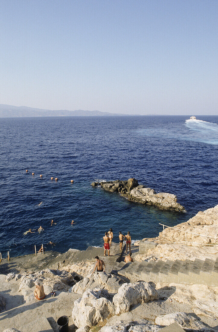 Young men swimming in the sea and jumping from rocks, Hydra, Hydra island, Mediterranean Sea, Greece, Europe