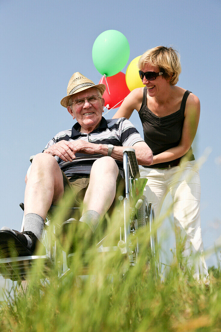 Woman wheeling senior man in a wheelchair, lake Kulkwitzer See, Leipzig, Saxony, Germany