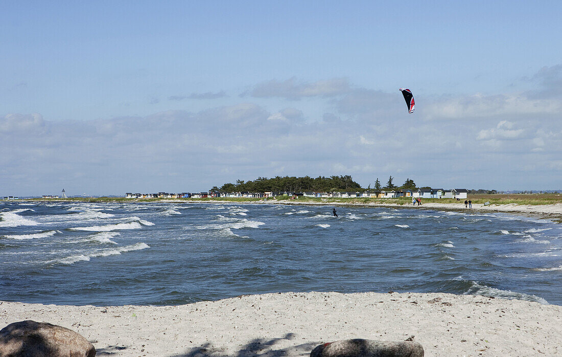 Kitesurfer mit Strandhäuschen im Hintergrund am Strand von Skanör, Skanör, Schonen, Südschweden, Schweden