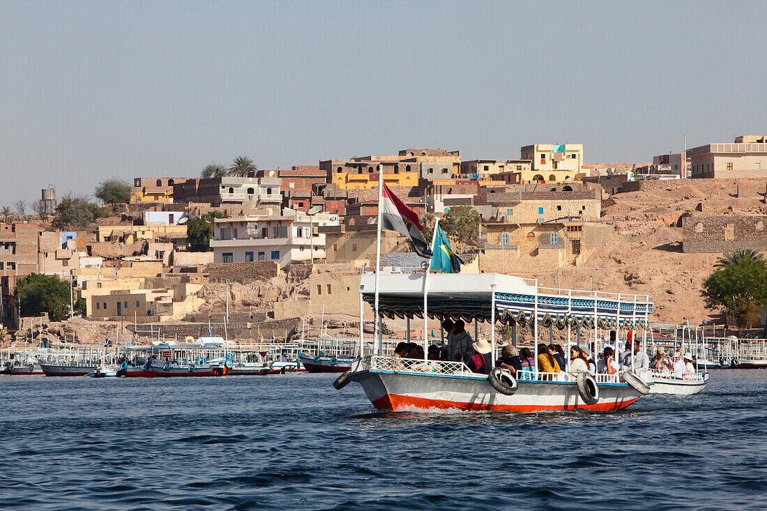Tourist boat on its way to the temple of Philae, a nubian settlement in the background, Aswan, Egypt, Africa