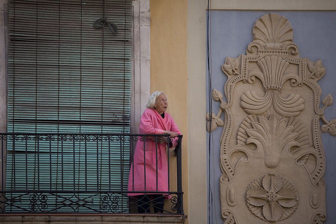 Alte Frau mit einer rosa Bademantel auf einem Balkon wegsehend