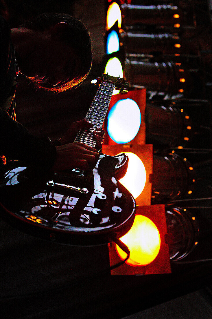 Young man playing electric guitar with floodlights in the background