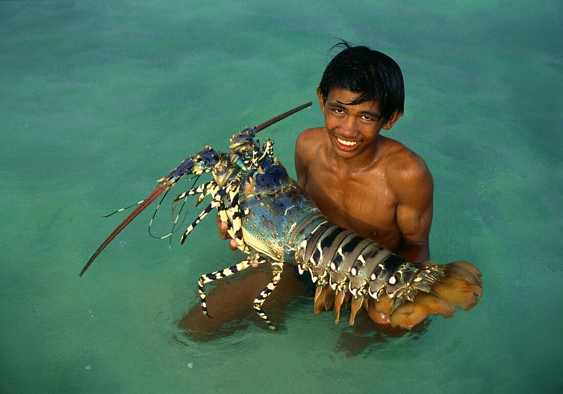 Junge im Wasser hält einen riesigen Hummer auf den Armen, Cebu Insel, Visayas, Philippinen, Asien