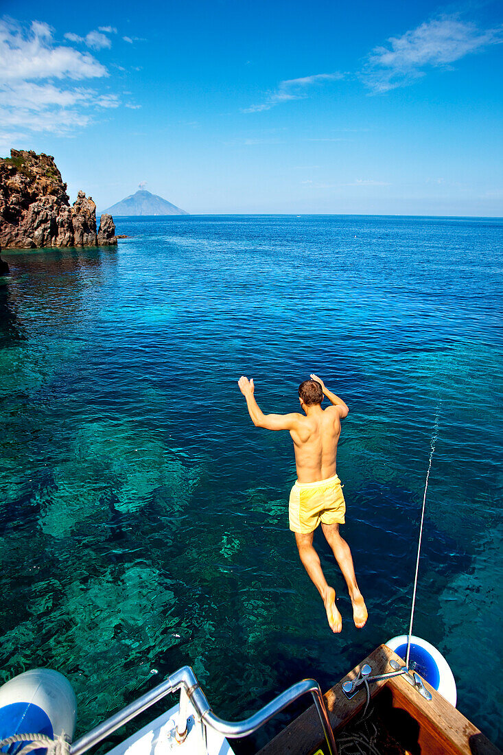Man jumping into the sea, Panarea Island, Stromboli in background, Aeolian islands, Sicily, Italy