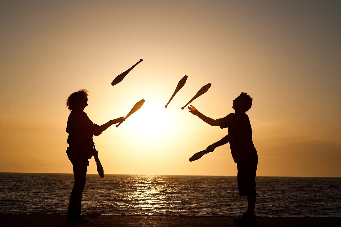 Two people juggling with clubs at sunset on Aberystwyth promenade wales UK