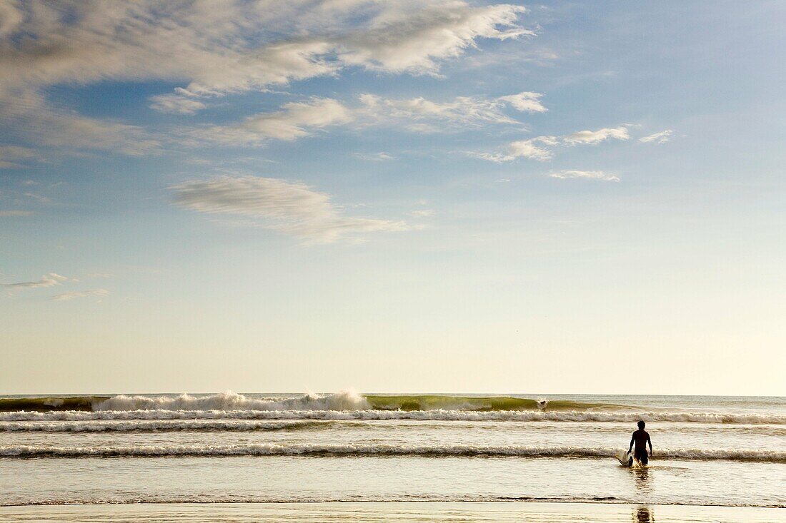 Surfer carrying his surfboard into the ocean in Dominical, Costa Rica