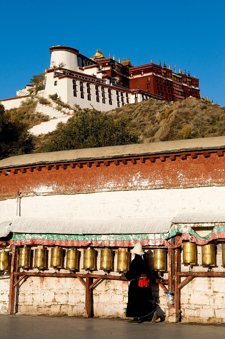 A Tibetan pilgrim walks around the Potala Palace in Lhasa Tibet while turning prayer wheels