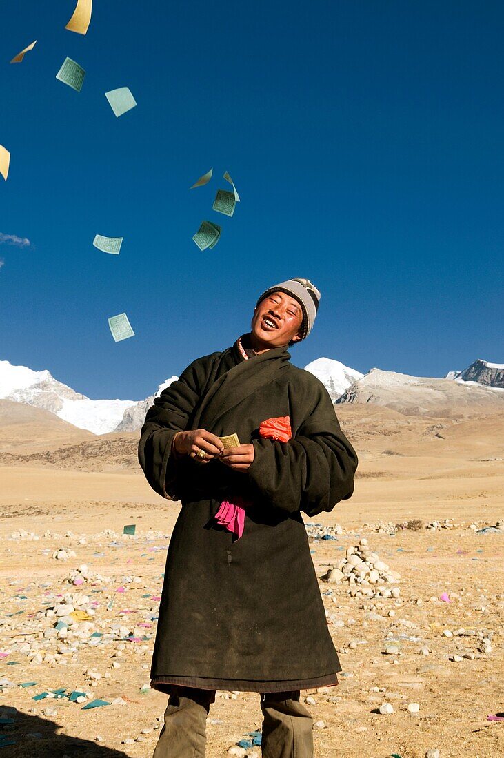 A Tibetan man throws paper wishes and prayers into the air in Tibet