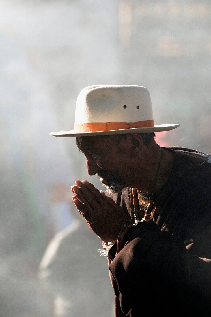 A tibetan man prays in the haze of the incense burner in front of the Jokhang temple in Lhasa Tibet