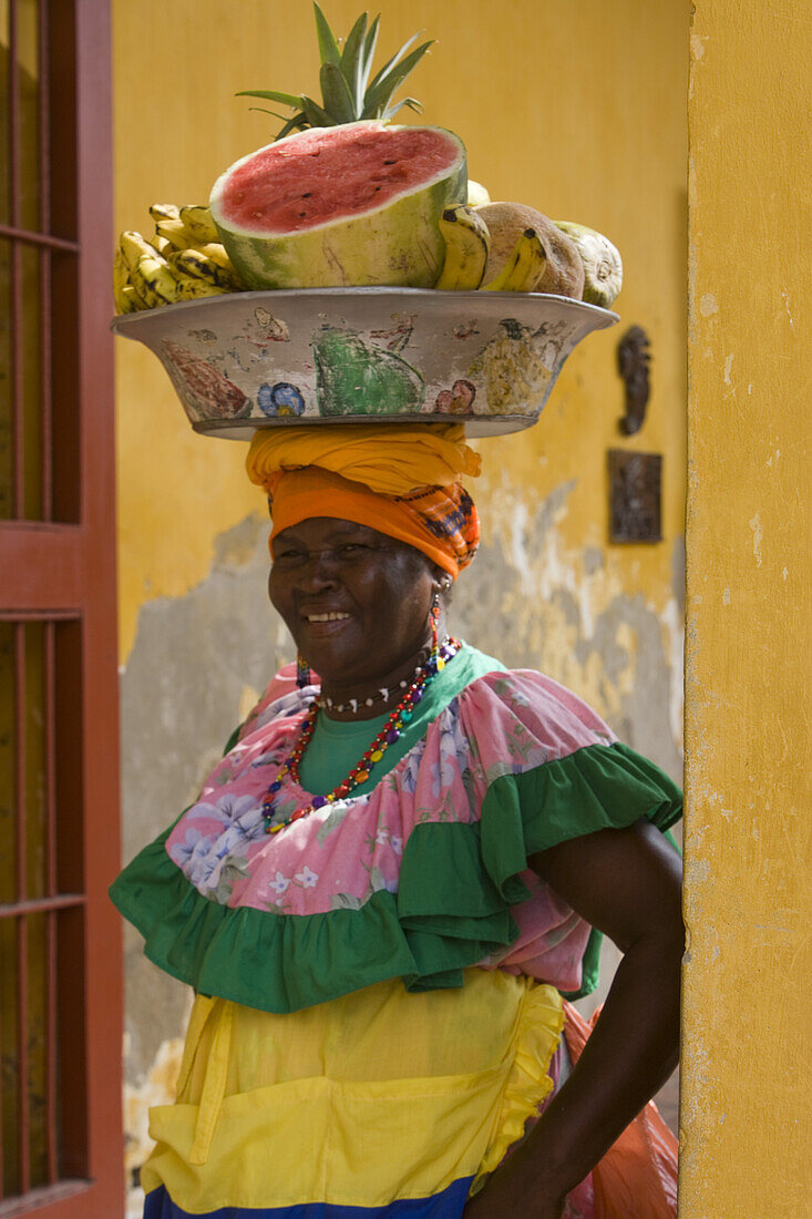 Frau in buntem, traditionellen Gewand trägt Schale mit Obst auf ihrem Kopf, Cartagena, Bolivar, Kolumbien, Südamerika