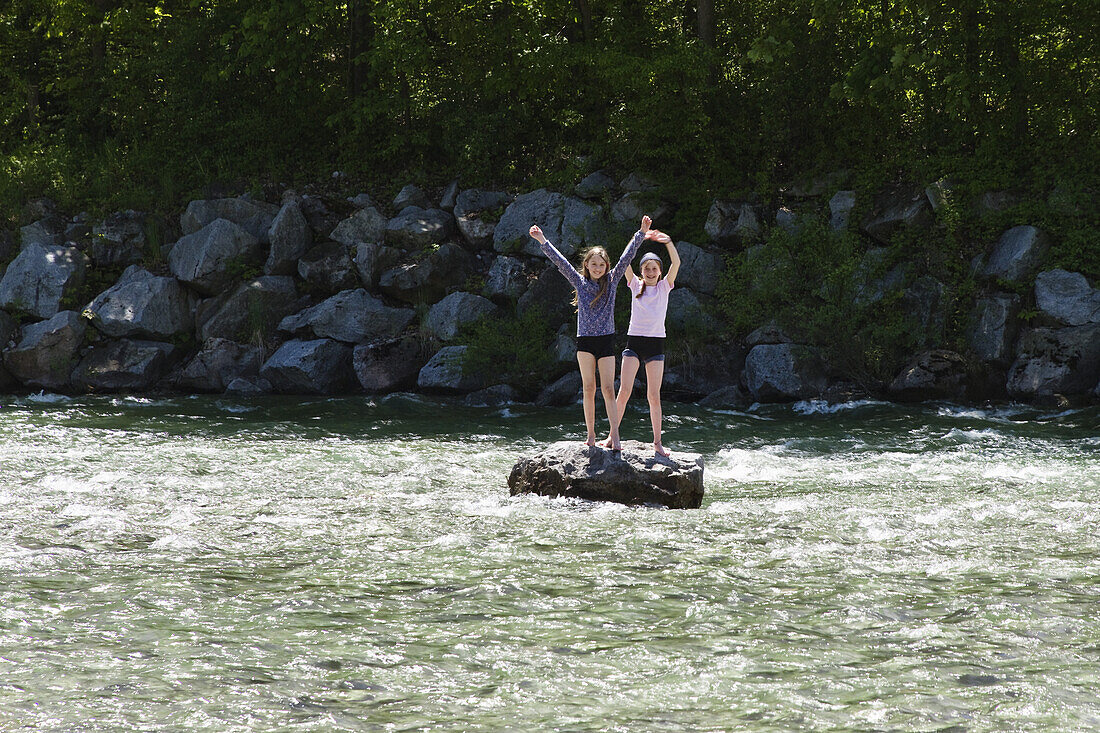 Zwei Mädchen (10 Jahre) stehen auf Felsen in der Isar, bei Fleck, Isarradweg, Oberbayern, Deutschland