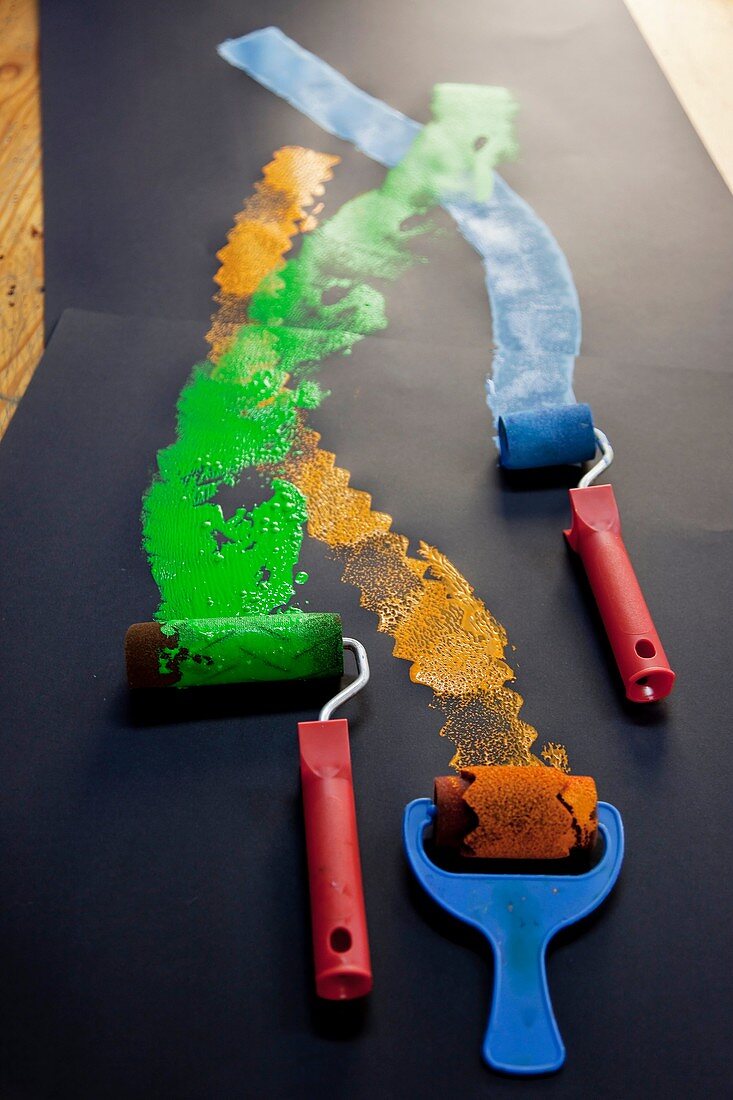 Primer plano de tres rodillos de pintura con colores verde, azul y naranja / Closeup of three paint rollers green, blue and orange colors