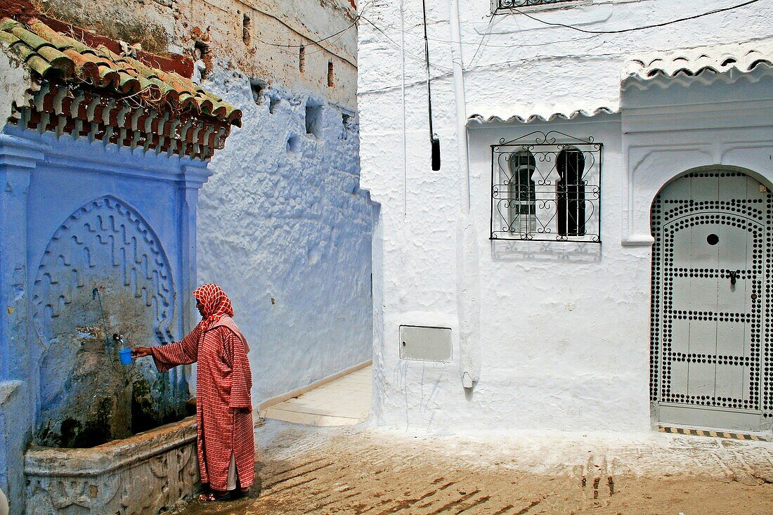 Moroccan woman taking water from a fountain, Chefchaouen, Morocco