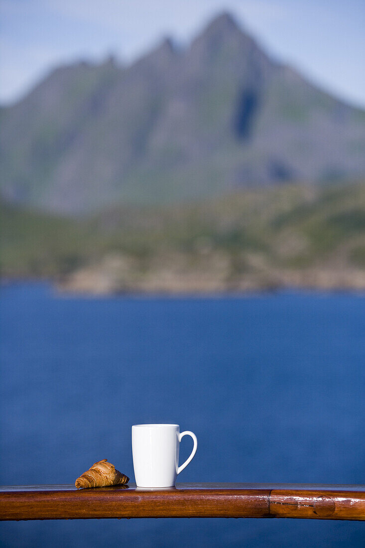 Croissant und Kaffeetasse zum Frühaufsteher-Frühstück an Bord von Kreuzfahrtschiff MS Astor (Transocean Kreuzfahrten), nahe Leknes, Lofoten, Norwegen, Europa