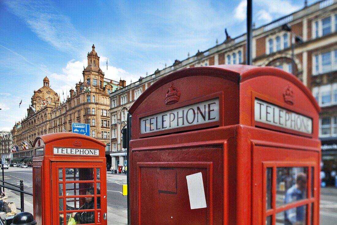 Typical red telephone boxes on Brompton Road with Harrods building on the background  London, England, United Kingdom