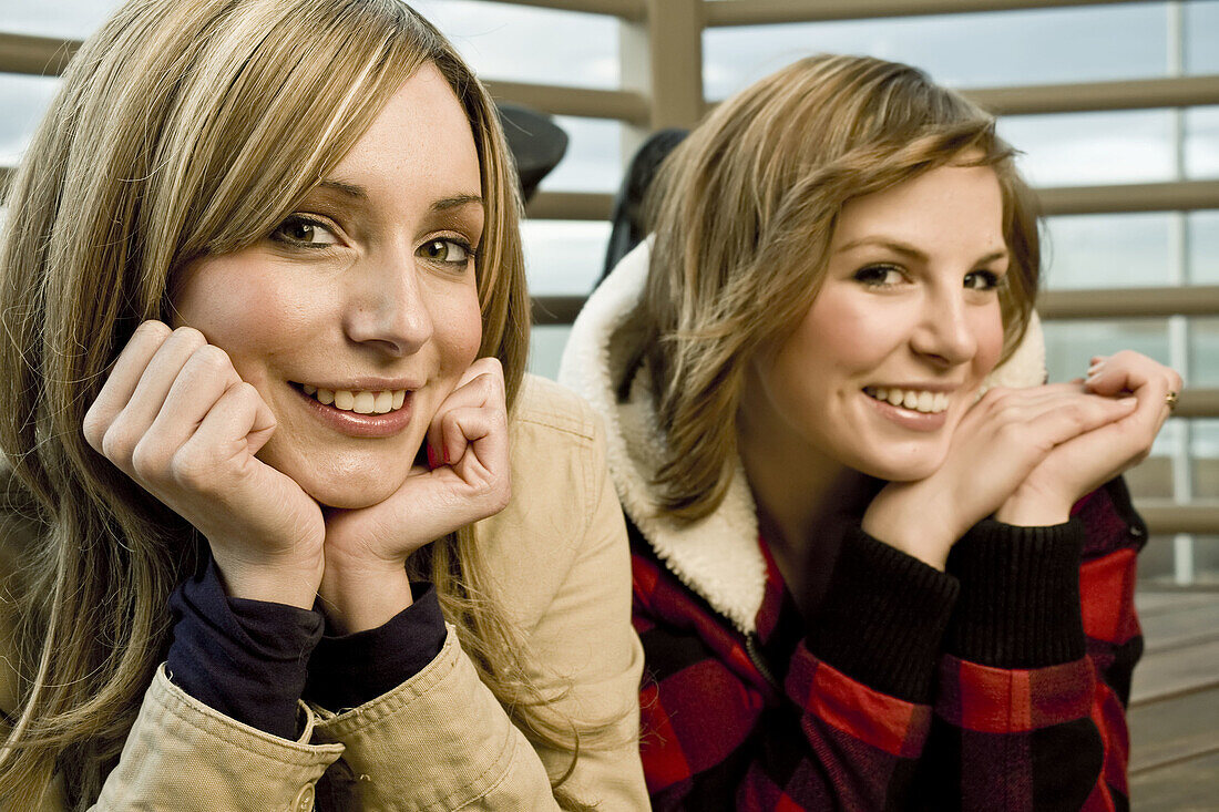 Two pretty young women rest their chins in their hands and smile for the camera