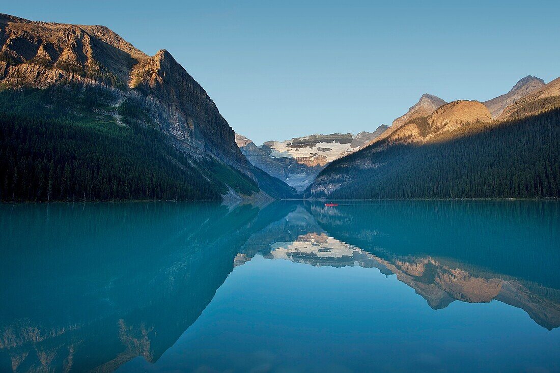 Man in red canoe paddling on Lake Louise at sunrise in Banff National Park, Alberta