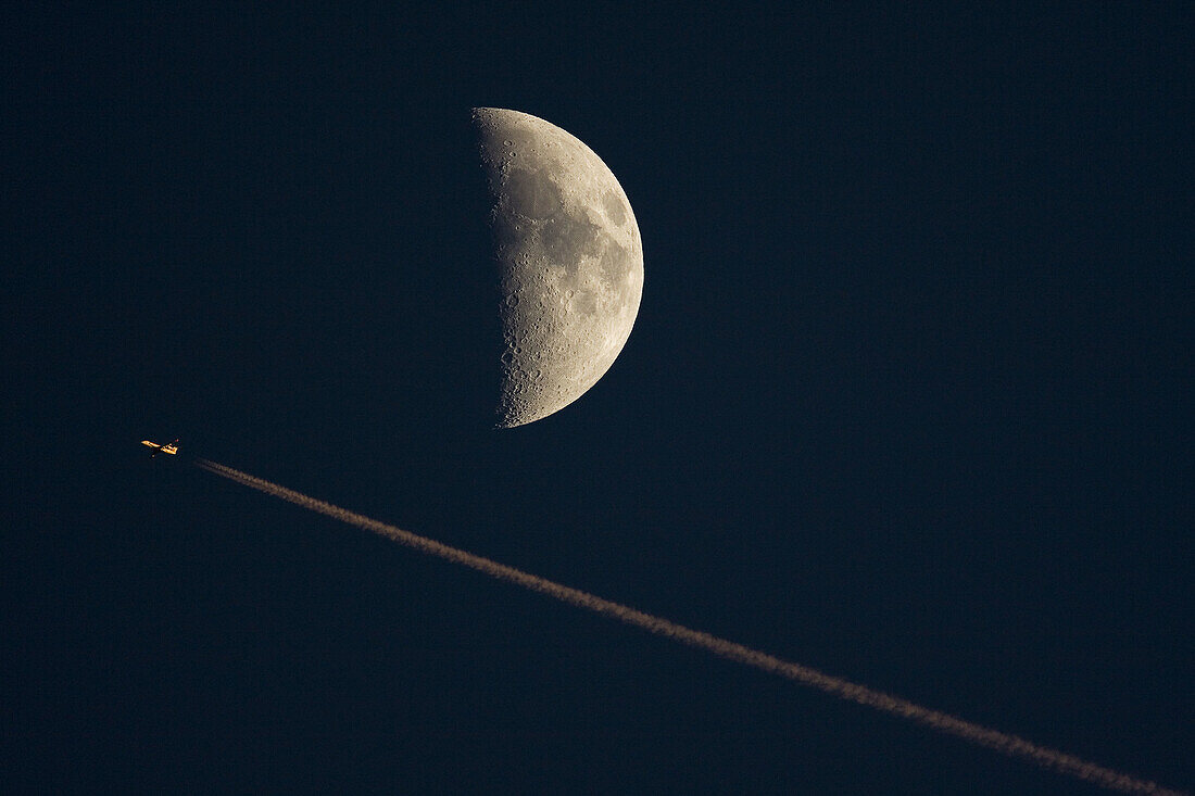 Plane, condensation trail and first quarter moon