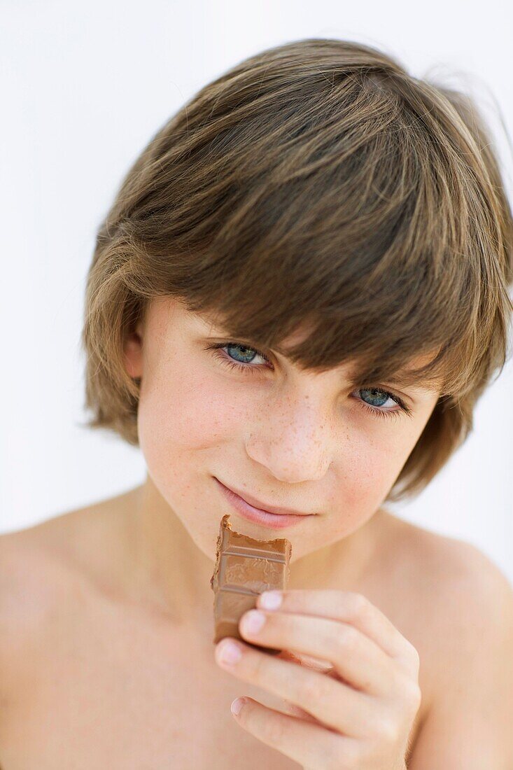 blue eyes, boy, brown hair, Caucasian ethnicity, chestnut hair, child, chocolate, Chocolate bar, Close-up, Color image, contemporary, eating, face, food, hand, headshot, holding, human, kid, looking at camera, Male, nourishment, one, one person, people, p