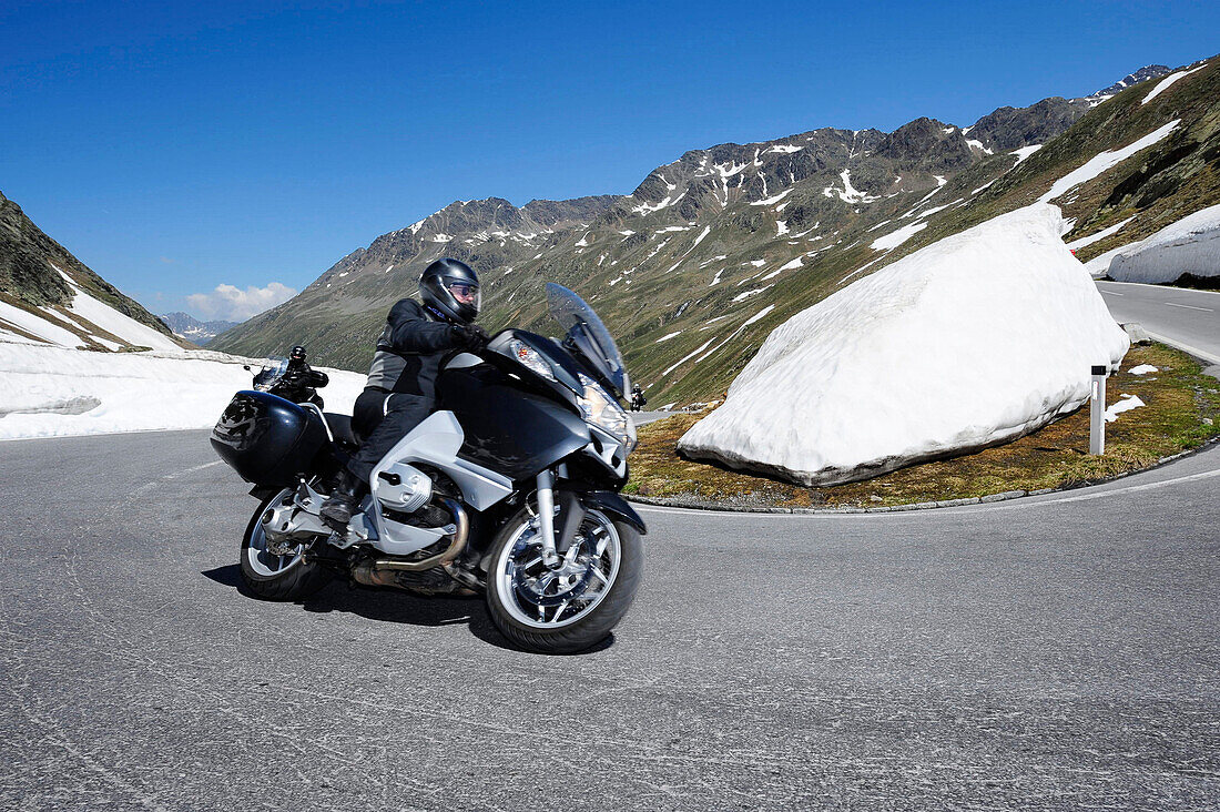 Motorradfahrer fährt Serpentine am Timmeljoch, Altschnee im Hintergrund, Timmelsjoch, Ötztal, Tirol, Österreich