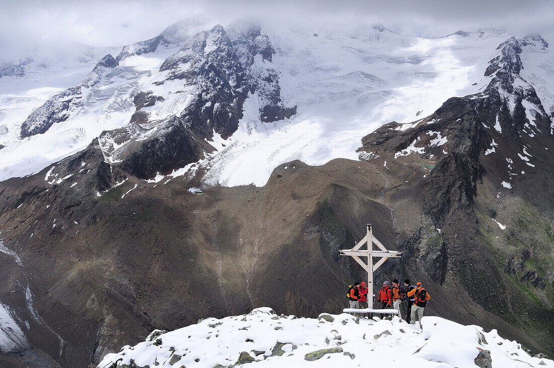 Group of mountaineers standing at a cross on the summit of Vorderer Schmied, valley of Langtauferer Tal, Vinschgau, Oetztal range, South Tyrol, Italy