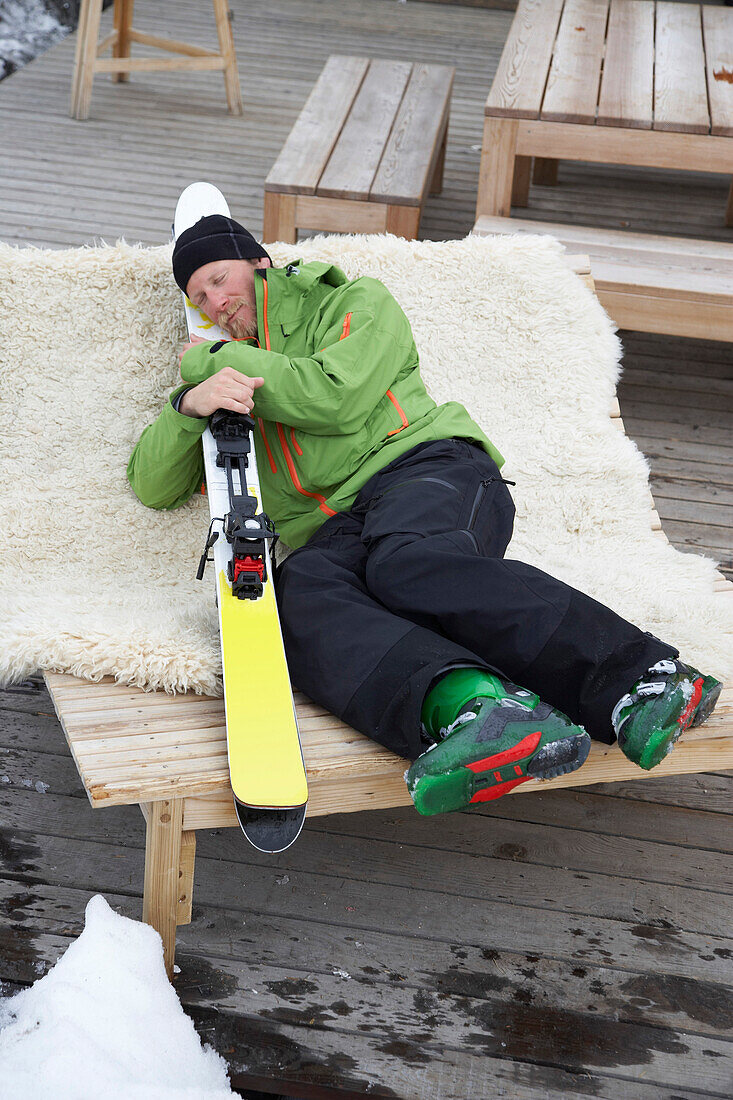 Skifahrer liegt mit Ski im Arm auf einer Sonnenliege, Flims, Kanton Graubünden, Schweiz