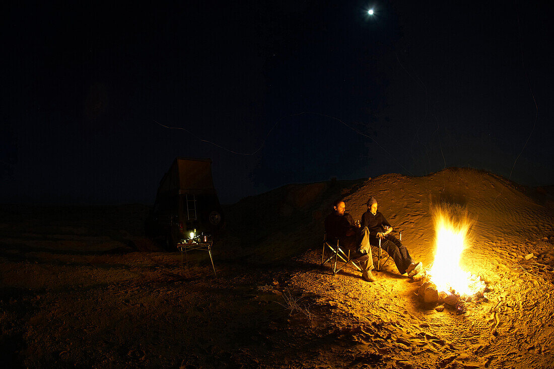 Couple sitting by the campfire at full moon, Chott El Jerid, Douz dune, Tunesia, Africa