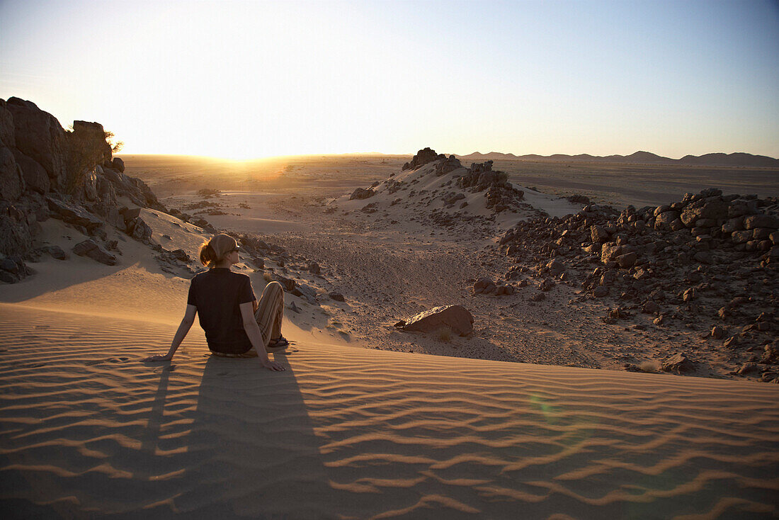 Frau sitzt auf Düne im Sonnenuntergang, Sudan, Afrika